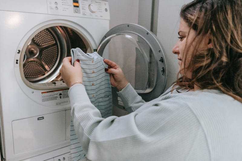 Woman holding a baby cloth in front of washing machine 
