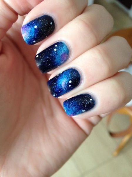 Celestial nail design with deep blues, galaxies, and shimmering stars.