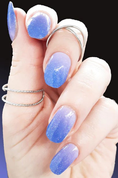 Sparkling stardust-inspired nails transition from lavender to blue brilliance.