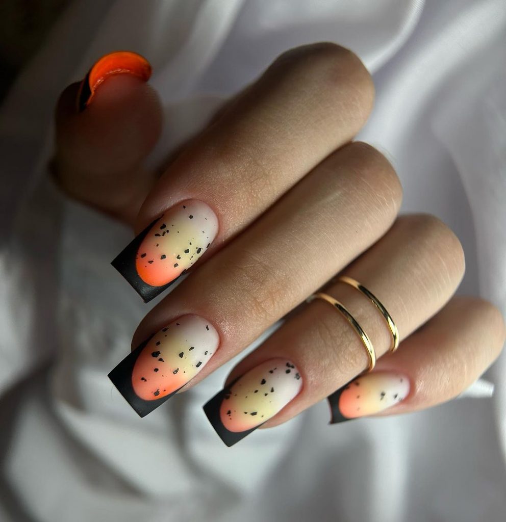 Black speckled nails with yellow-orange ombre.