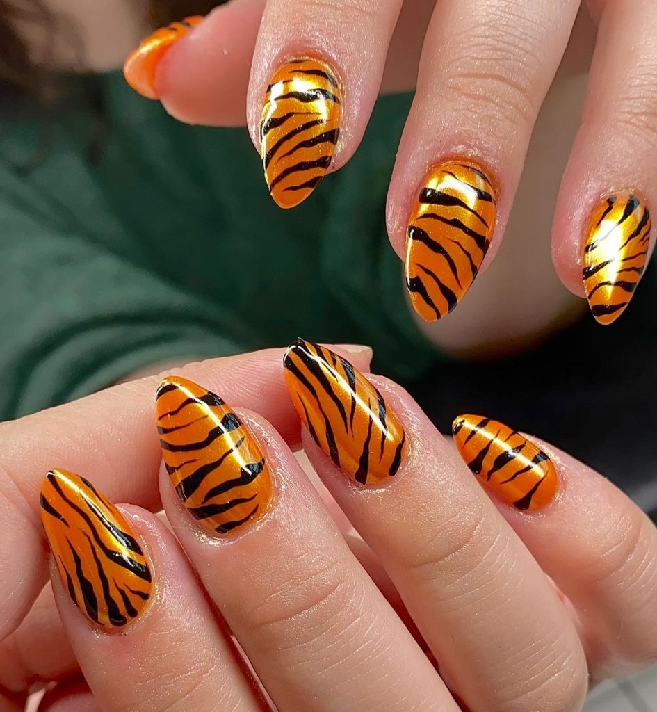 Tiger print on yellowish-orange chrome nails.