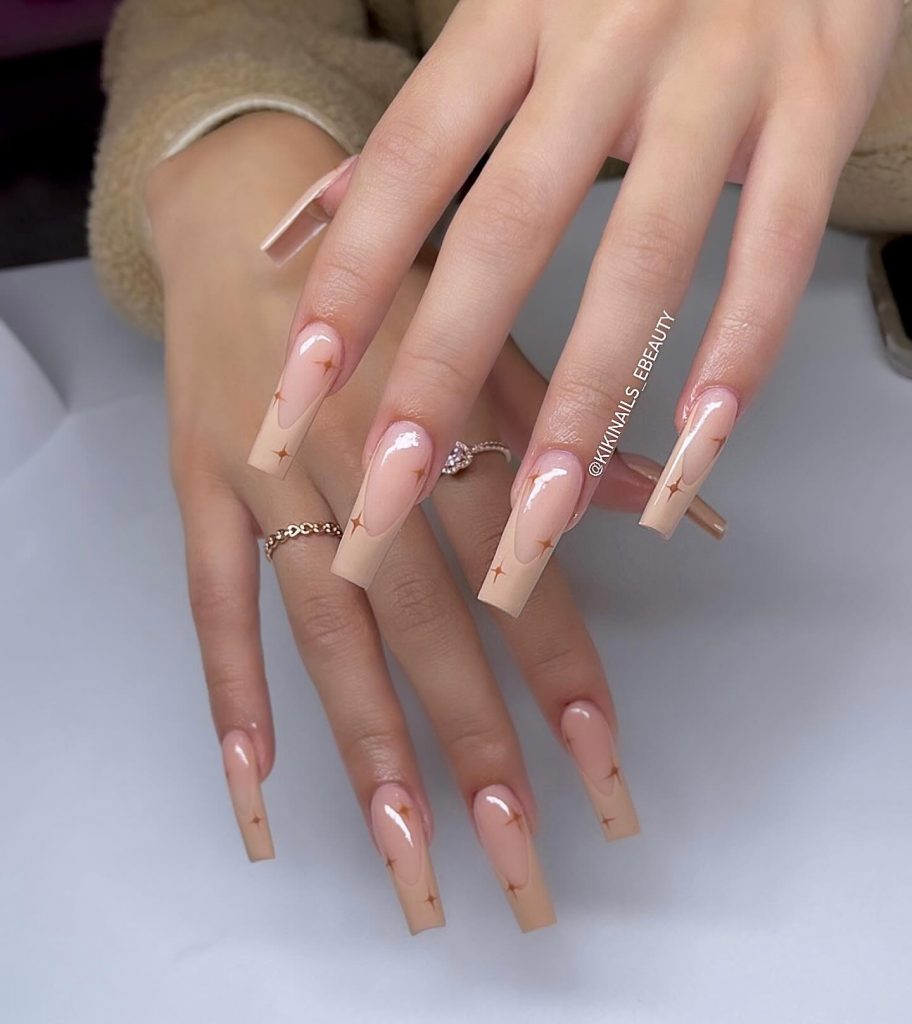 Nude French tip and glossy clear nails with brown stars.