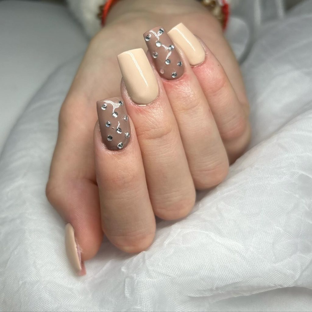 Square nails with shades of beige and gemstone embellishments.